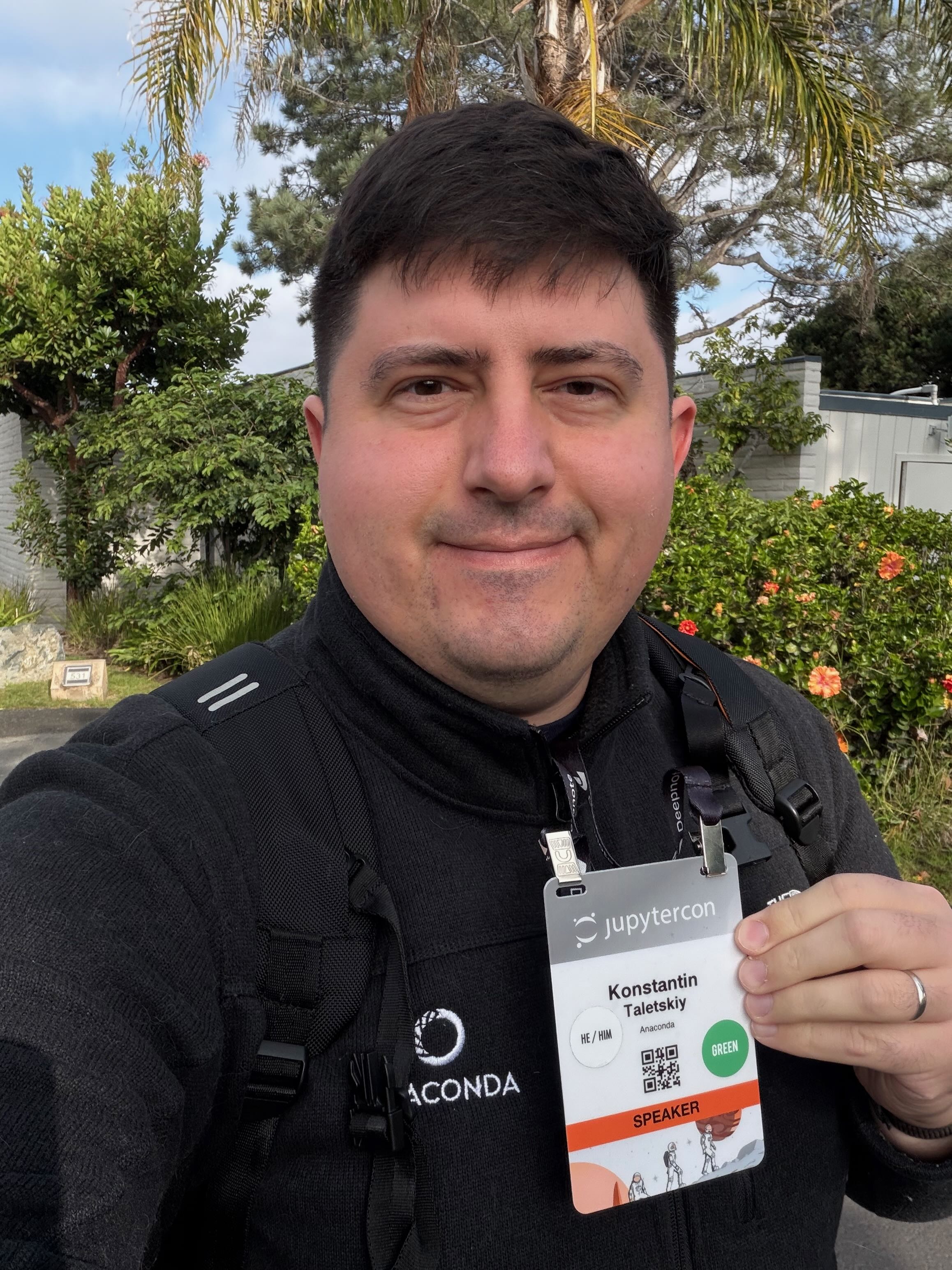 Me at JupyterCon 2025, wearing Anaconda jacket and showing my badge
